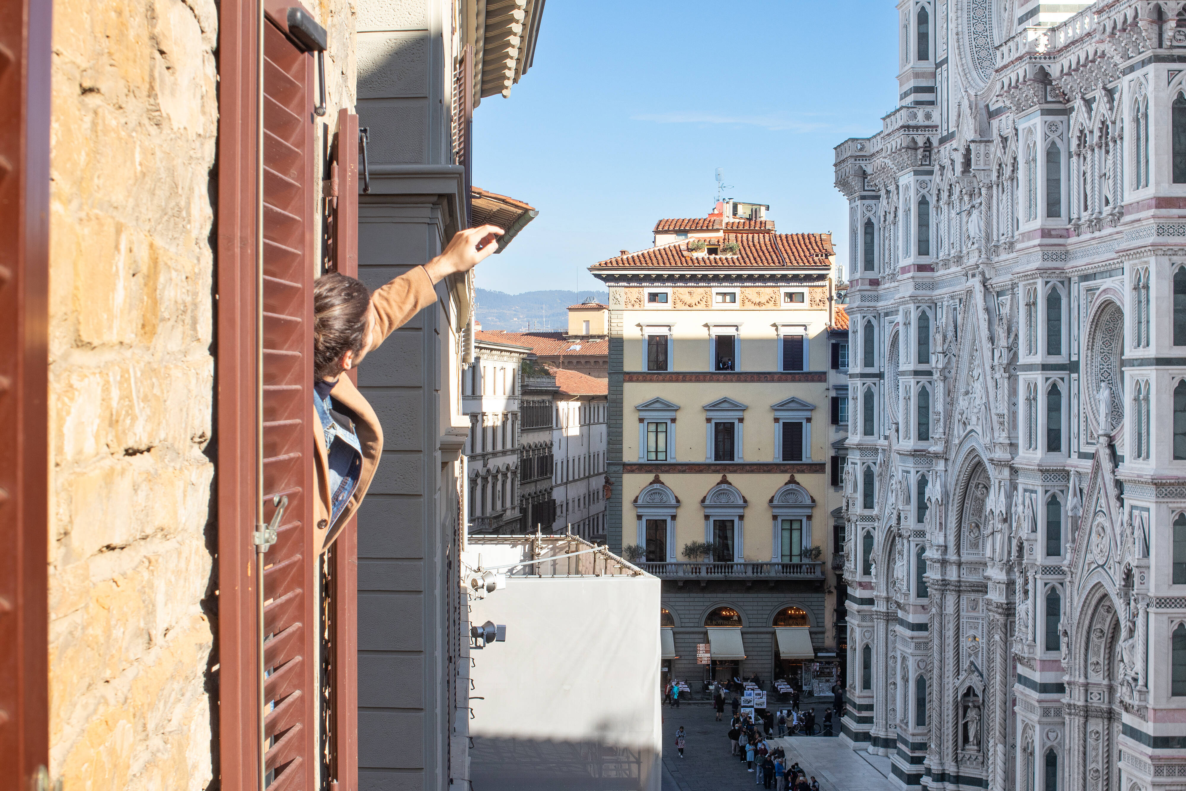 Urban parkour athlete scaling a historic building facade in Florence, Italy, with the iconic Duomo cathedral visible in the background. The image captures a daring free-running move against classic Italian Renaissance architecture, featuring ornate buildings with terracotta roofs and traditional Florentine windows. The contrast between modern street sports and centuries-old architecture creates a striking juxtaposition in the heart of Florence's historic center.